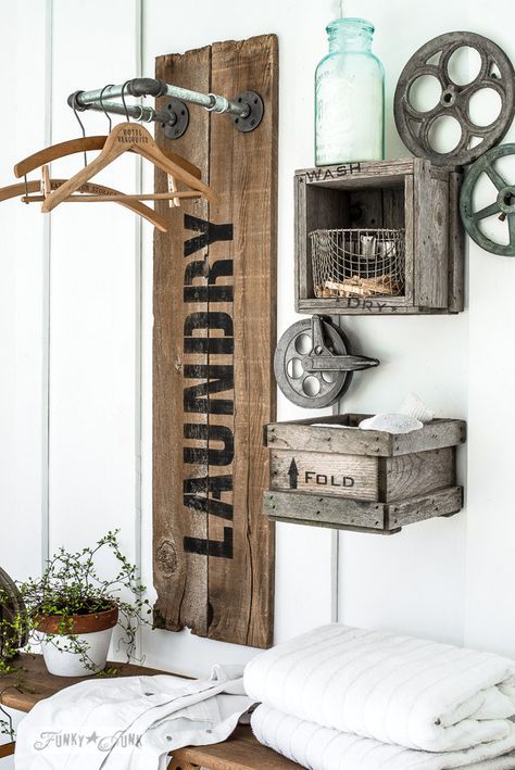 an industrial laundry space with a reclaimed wood shelf with pipes and clothes hangers, crates for storage and metal wheels