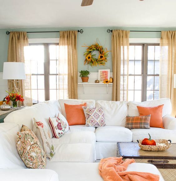 bright orange textiles, bright fall blooms and a sunflower wreath bring a fall feel to the neutral living room