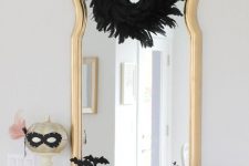 glam Halloween styling with a black feather wreath, a gold pumpkin in a mask, pink and white pumpkins and black bats