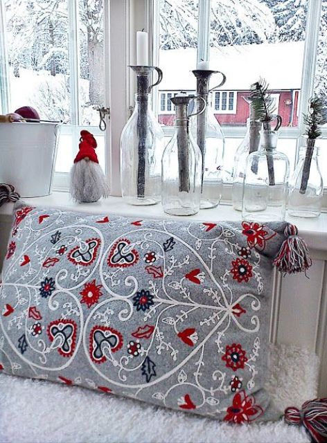Scandi Christmas decor with a grey embroidered pillow, a gnome in a red hat, bottles with candleholders and evergreens