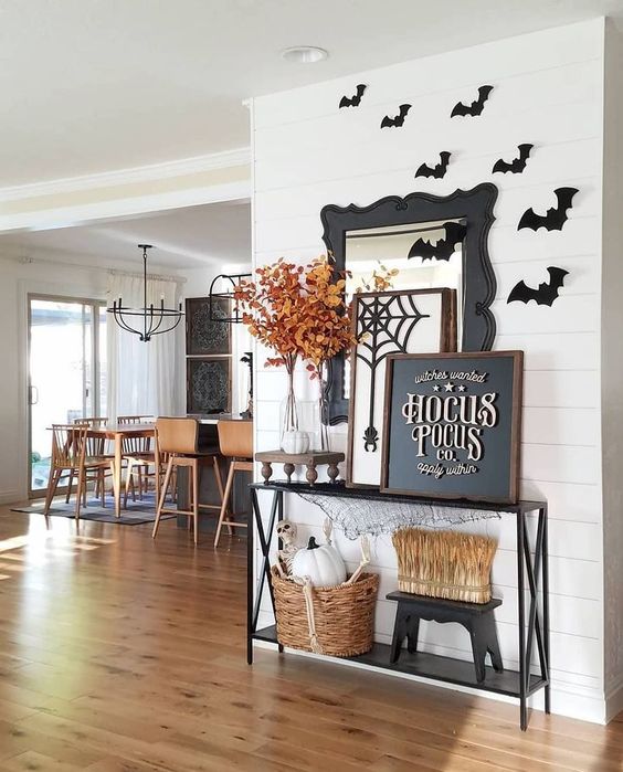 a Halloween console table with wheat and pumpkins, fall leaves in a glass vase, a chalkboard sign, black paper bats