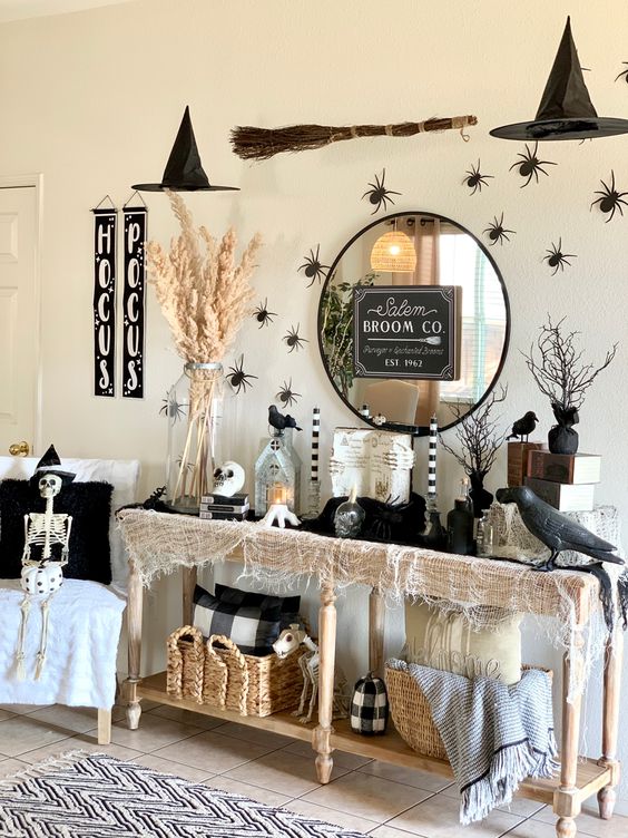 a Halloween console with neutral cheesecloth, blackbirds, spiders, a round mirror, lanterns and candles and pampas grasses