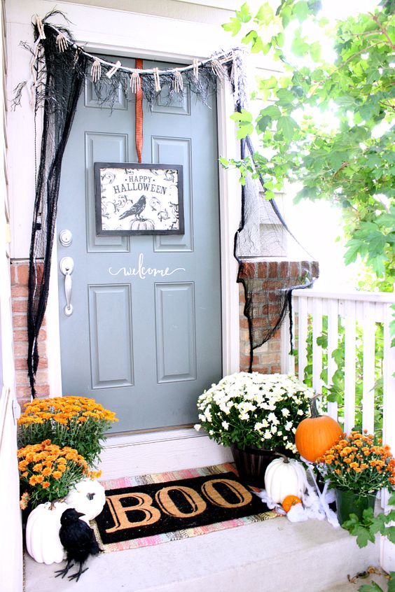 a Halloween front door with a black sign, skeleton hands and black spiderweb, a black mat and a blackbird plus pumpkins