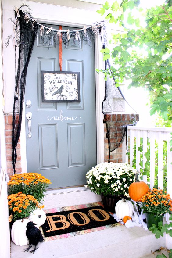 a Halloween front door with a black sign, skeleton hands and black spiderweb, a black mat and a blackbird plus pumpkins