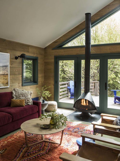 a beautiful modern living room with a black Malm fireplace, a burgundy sofa, a printed orange rug, neutral chairs, a round wooden coffee table