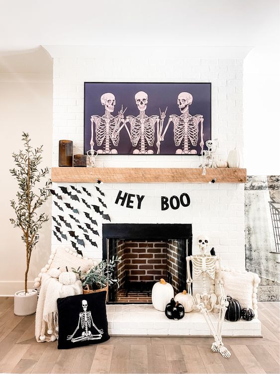 a black and white Halloween mantel with a letter banner, black paper bats, black and white pumpkins, a skeleton and potted plants