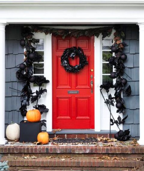 a black feather wreath, black ornaments, leaves and feathers framing the door, white and orange pumpkins for Halloween decor