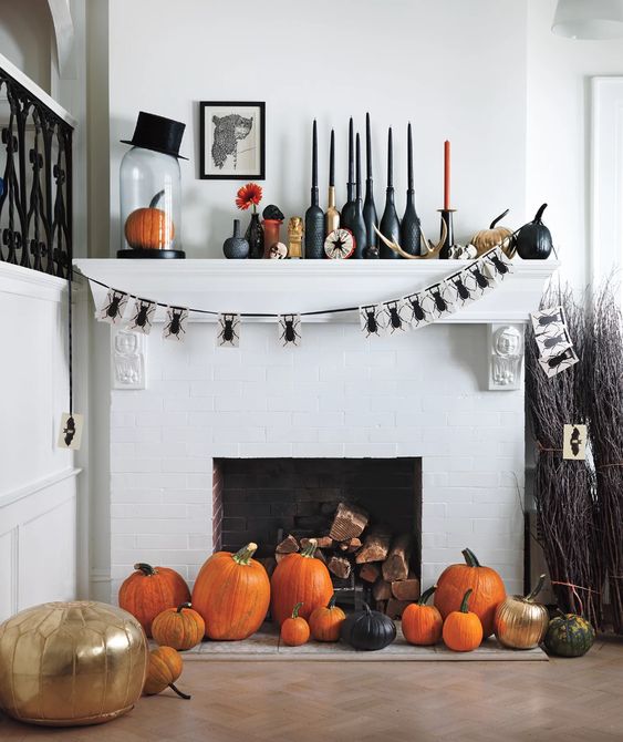 a bold Halloween mantel with a bug garland, colorful candles, bold orange, black and gold pumpkins, a top hat and an artwork