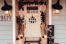 a bold Halloween porch with hay, orange, white and black pumpkins, bold blooms, corn husks, witches’ hats and evergreens