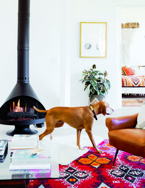 a bold mid-century modern living room with a black Malm fireplace, a bright printed rug, a leather chair, a low coffee table