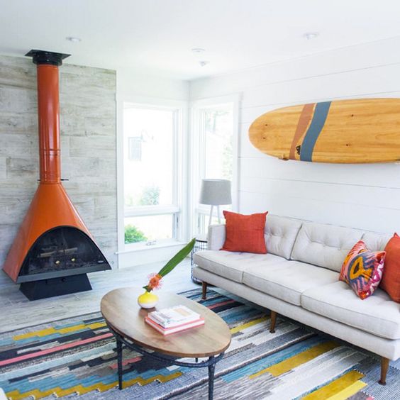 a bold modern living room with an orange Malm fireplace, a grey sofa, a low coffee table, a colorful rug and pillows