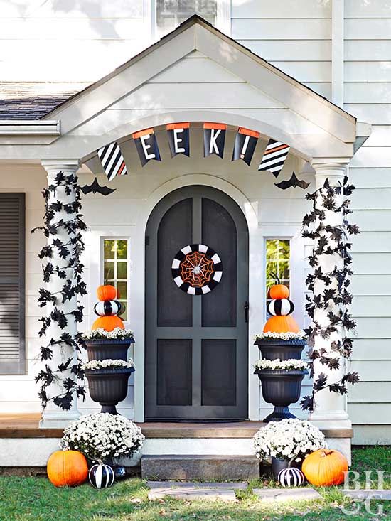 a bright and cool Halloween front porch with black leaves covering the pillars, orange and black and white pumpkins, a spiderweb sign