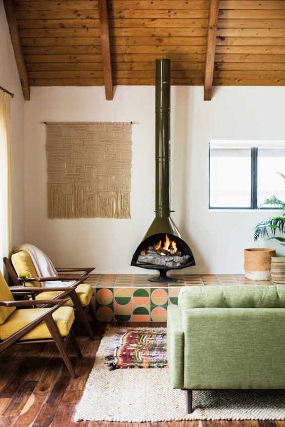 a bright boho meets modern living room with a dark green Malm fireplace, bright tiles, a green sofa and yellow chairs