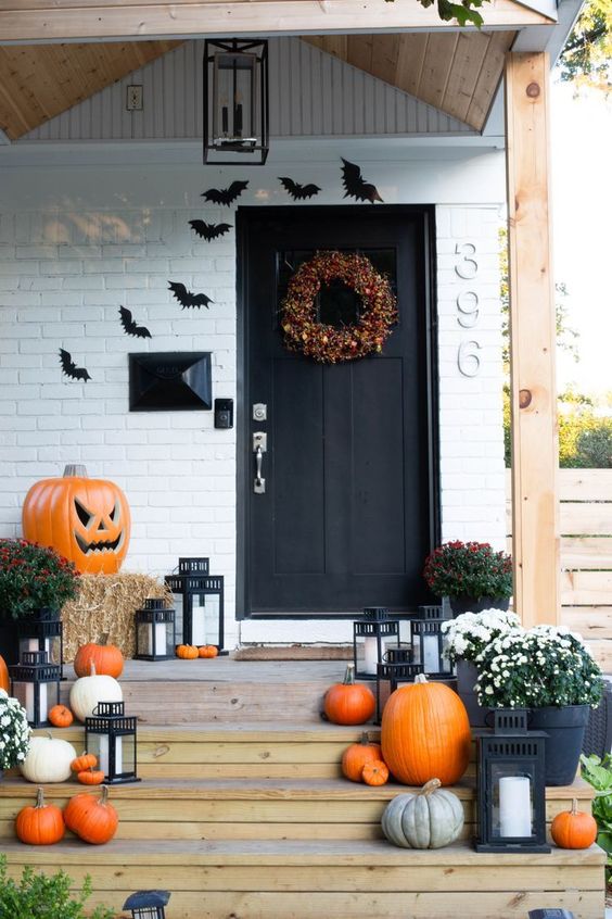 a bright rustic Halloween porch with bold and pastel pumpkins, blooms, hay, a giant jack-o-lantern, bats and a catchy fall-colored wreath