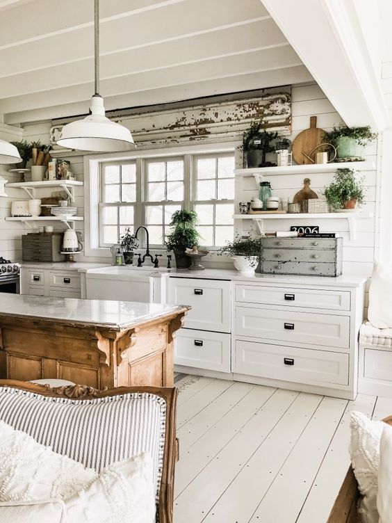 a charming white cottage kitchen with planked walls, shaker cabinets, corbel shelves and pendant lamps plus greenery