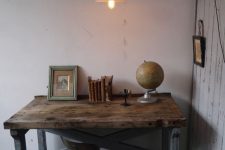 a chic home office with white shabby walls, an industrial desk of aged wood and metal legs plus a metal sconce on the wall