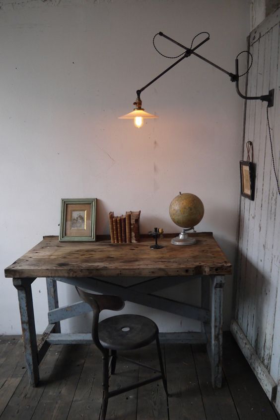a chic home office with white shabby walls, an industrial desk of aged wood and metal legs plus a metal sconce on the wall