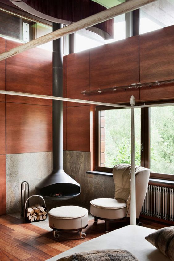 a chic modern sitting nook with a grey suspended Malm fireplace, a neutral chair and a footrest and a firewood stand