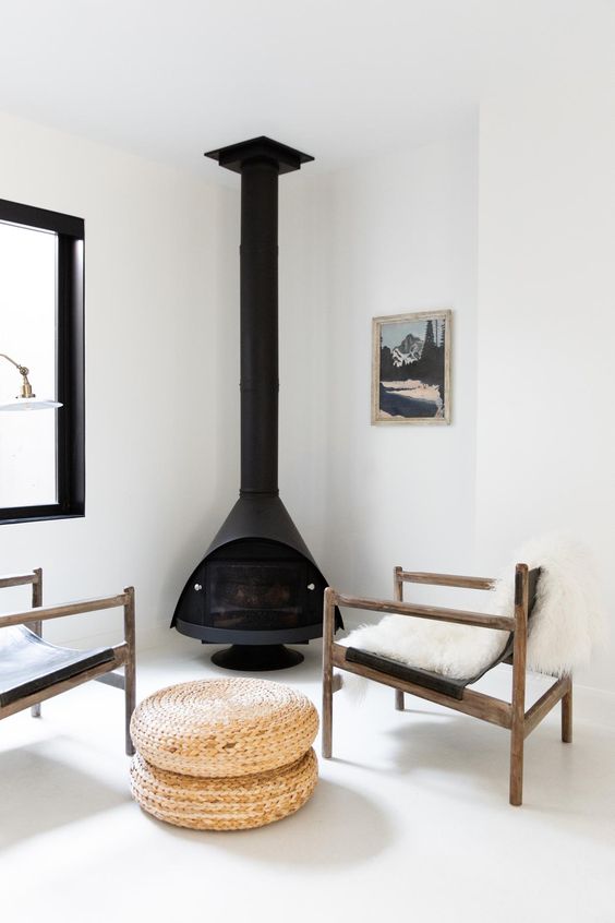a clean and chic sitting nook with a black Malm fireplace, black leather chairs, jute poufs and all white everything around