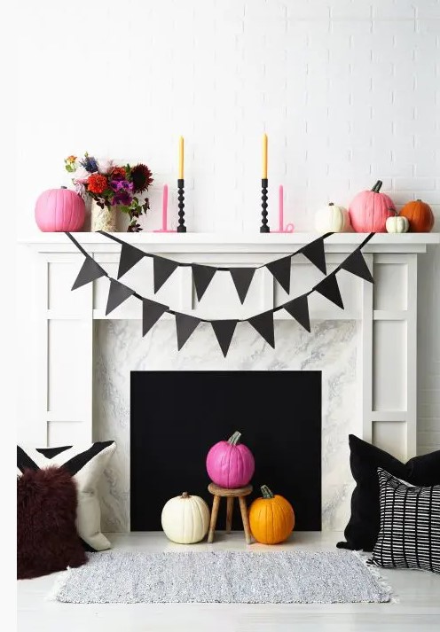 a colorful fireplace and mantel with bright candles, pumpkins and flowers in a vase for Halloween