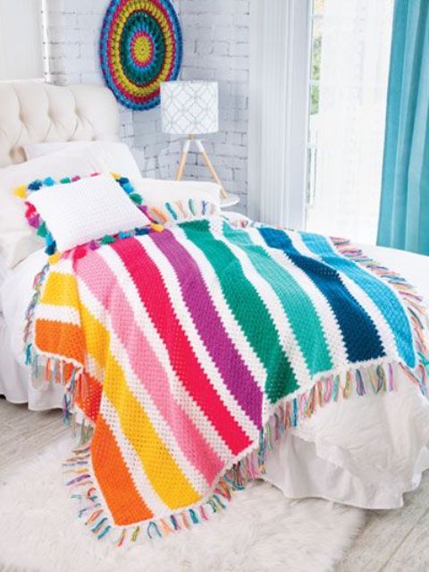 a colorful striped crochet blanket with tassels and matching pillow cases with tassels for adding fun to the bedroom