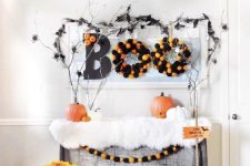a console table styled for Halloween in a bold and fun way, with black witches’ hats, fauxfur, pumpkins, wreaths and bold blooms, branches and spiders