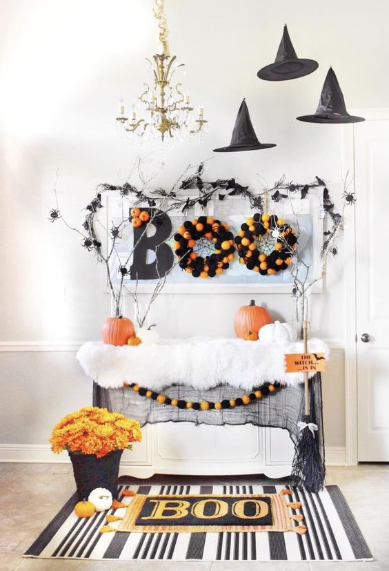 a console table styled for Halloween in a bold and fun way, with black witches' hats, fauxfur, pumpkins, wreaths and bold blooms, branches and spiders