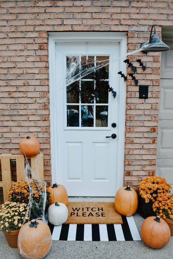 a cool Halloween porch with black bats on the door and walls, spiderweb, bold blooms and pumpkins and layered rugs