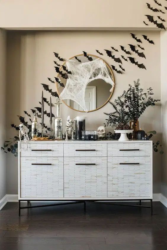a cool console table with black bats, greenery in vases, skulls and skeletons, spiderwebs is a gorgeous idea for Halloween