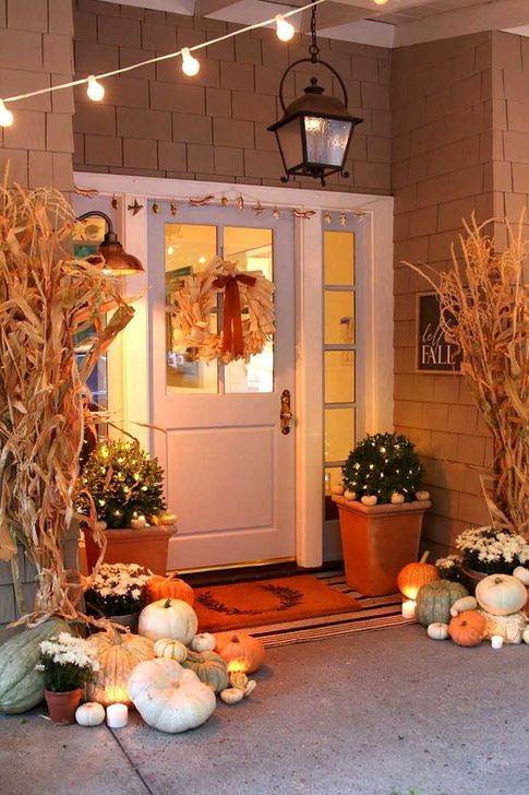 a corn husk wreath, greenery arrangeements with lights and white pumpkins, white blooms and heirloom pumpkins on the porch