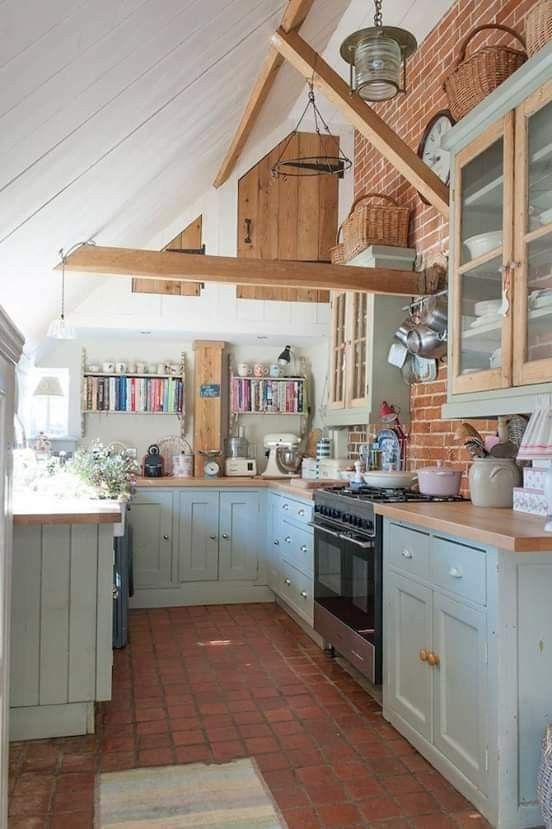 a cottage kitchen with wooden beams, ligth blue shaker cabinets, butcherblock countertops and a tile floor is cozy and cool