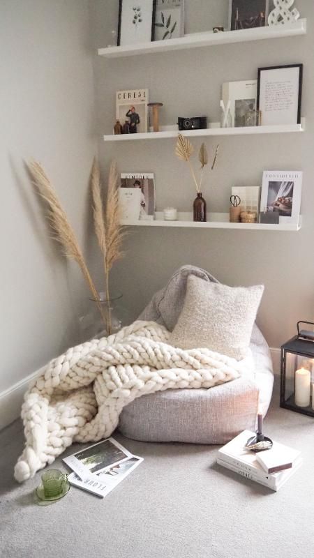 a cozy Nordic reading nook with open shelves, a beanbag chair, a chunky crochet blanket and a neutral pillow, some magazines and books