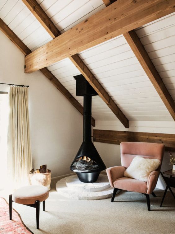 a cozy attic nook with a black Malm fireplace, a mauve chair and a footrest, a neutral rug and a pillow is a lovely space