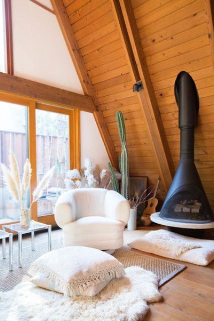 a cozy neutral sitting nook with a black Malm fireplace, a creamy chair, layered rugs and pillows, a glass coffee table and pampas grass