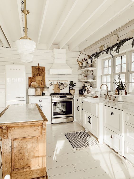 a cute cottage kitchen in white, with beadboard walls, shaker style cabinets, a stained kitchen island and wooden decor