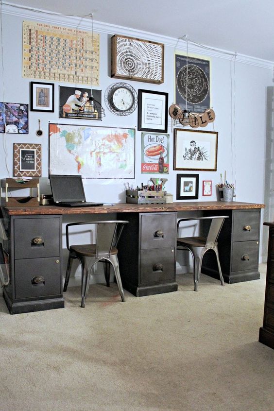 a double vintage industrial desk of metal and wood, with metal chairs and a large and bright gallery wall over it