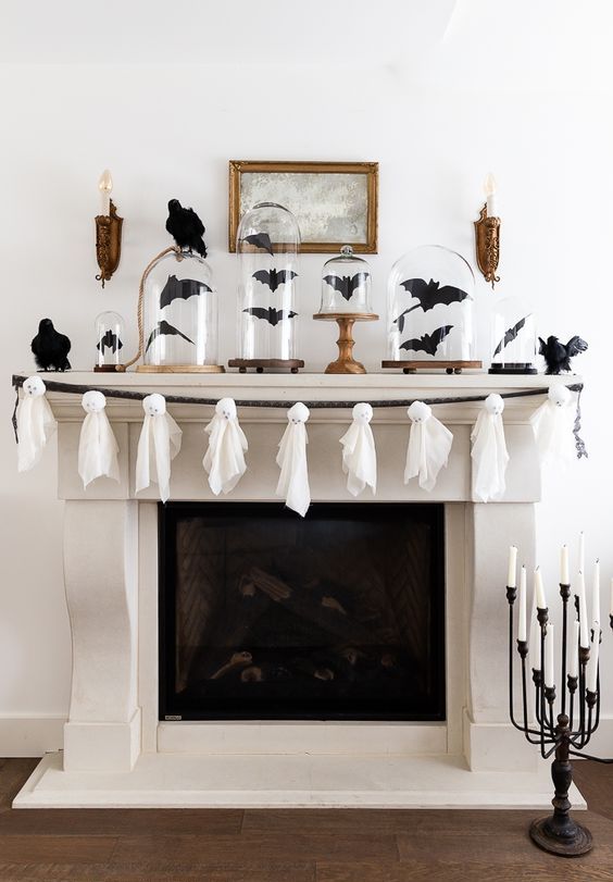 a fun Halloween mantel decorated with black bats in cloches and a garland of white ghosts is a cool idea for a holiday