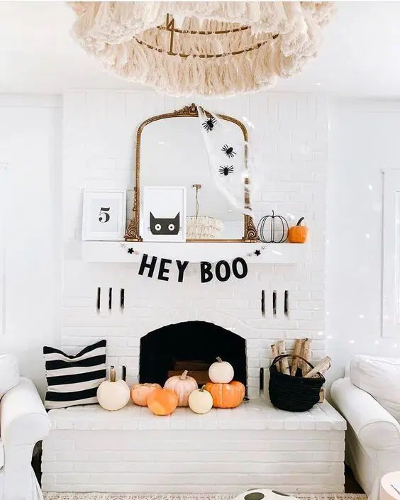 a fun modern Halloween fireplace with a letter banner, signs, pumpkins, firewood and a cat artwork plus some spiders on the mirror