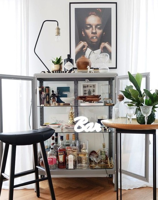 a glass bar cabinet with artworks, a lamp, some plants and a neon sign is a very chic idea