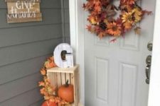 a lush fall leaf and bloom wreath with pinecones, crates with fall leaves and pumpkins for a Thanksgiving porch