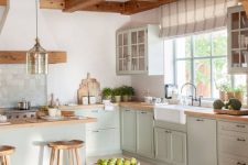 a modern cottage kitchen with wooden beams on the ceiling, light green shaker style cabinets, butcherblock countertops, a basket for storage and a pendant lamp