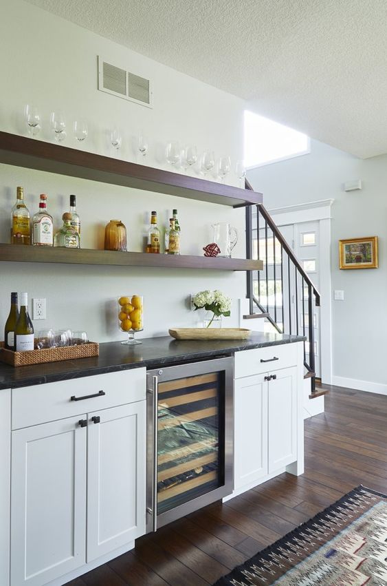 a modern farmhouse home bar with white shaker style cabinets, a black stone countertop, open shelves is an elegant idea to rock