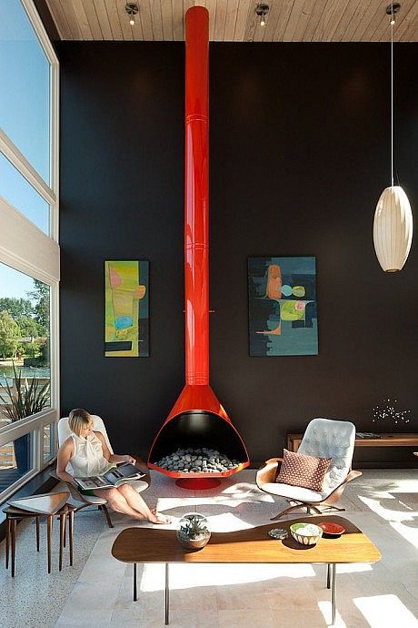 a modern living room with double-height ceilings, a black accent wall with artwork, white chairs, a brown couch and a coffee table plus an orange Malm fireplace