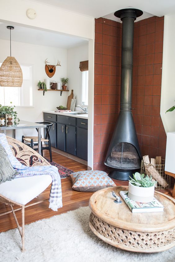 a modern meets boho sitting nook with a black Malm fireplace, a wooden coffee table, a wire basket for firewood and a chic chair