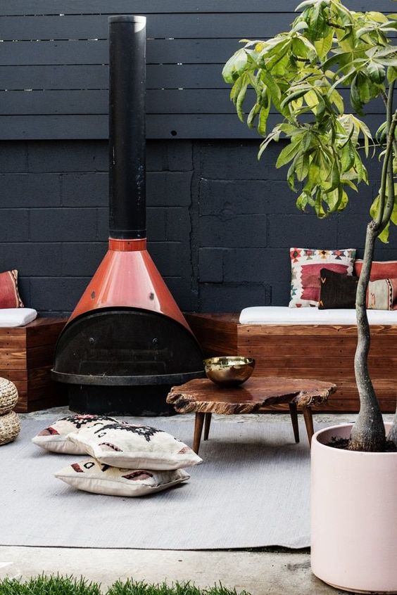 a modern outdoor space with stained furniture and bright pillows, a red Malm fireplace, a living edge coffee table and a potted plant