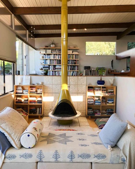 a modern sunken living room with a mustard Malm fireplace, stained bookshelves and a daybed with boho bedding is a cool space