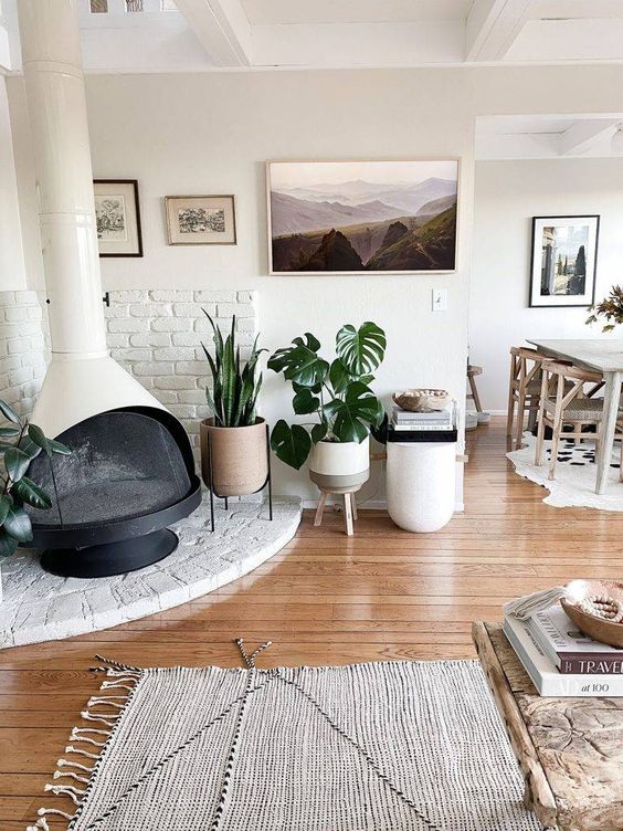 a neutral boho space with a white Malm fireplace, potted plants, a gallery wall, some rugs and lovely modern furniture