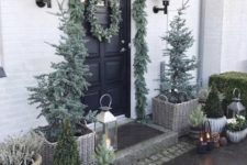 a pale winter front door with an evergreen garland and wreaths, Christmas trees, candle lanterns and pinecones