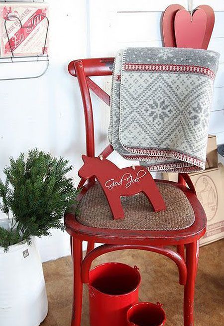 a red chair with a grey embroidered blanket, a red horse decoration, red buckets and some red hearts on the wall for Christmas