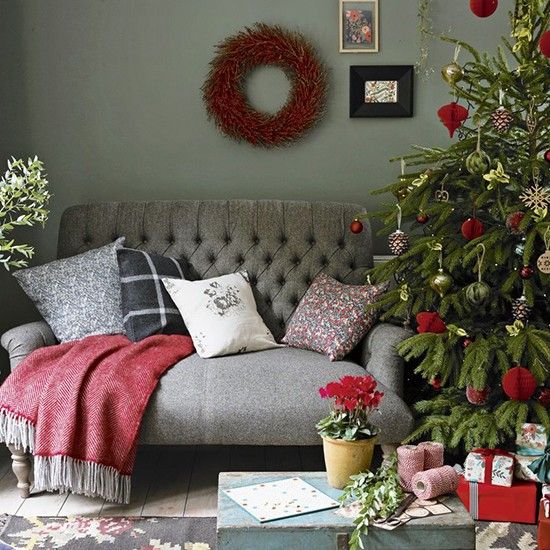 a red loveseat with red, grey and white pillows, a red blanket, a Christmas tree with red and green ornaments and a mini gallery wall